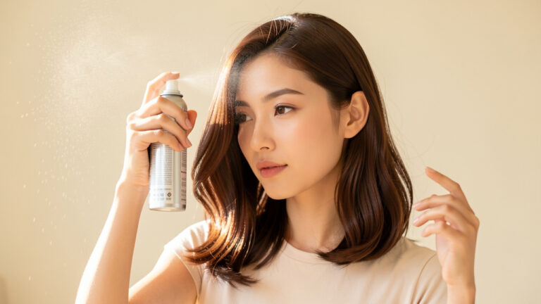 Une jeune femme applique délicatement de la laque sur une coiffure souple et volumineuse, sans effet carton.