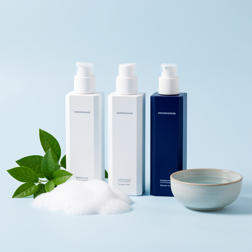 Trois flacons de soins capillaires dermatologiques blancs et bleu foncé présentés dans une composition lumineuse avec des feuilles vertes et de la mousse.
